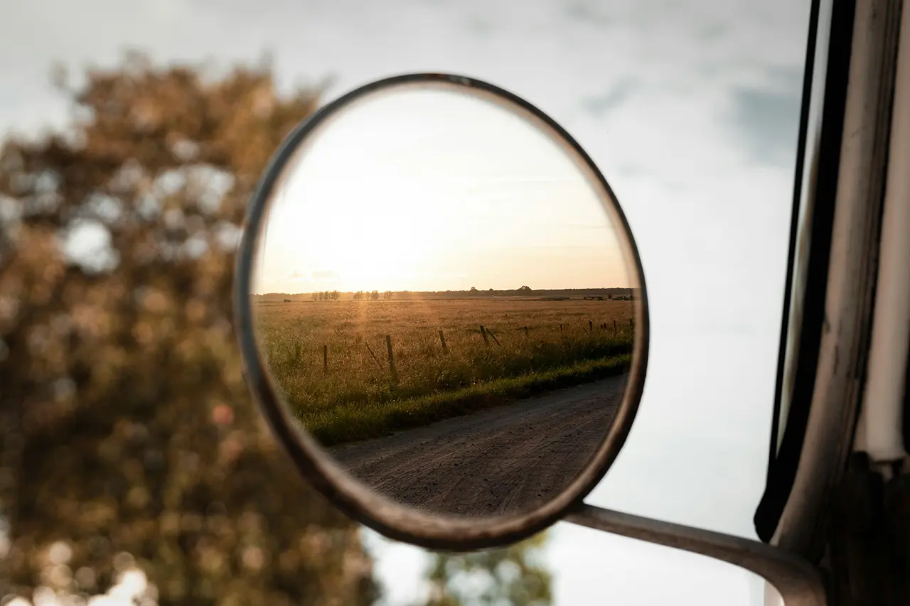 round side mirror overlooking open field at sunrise