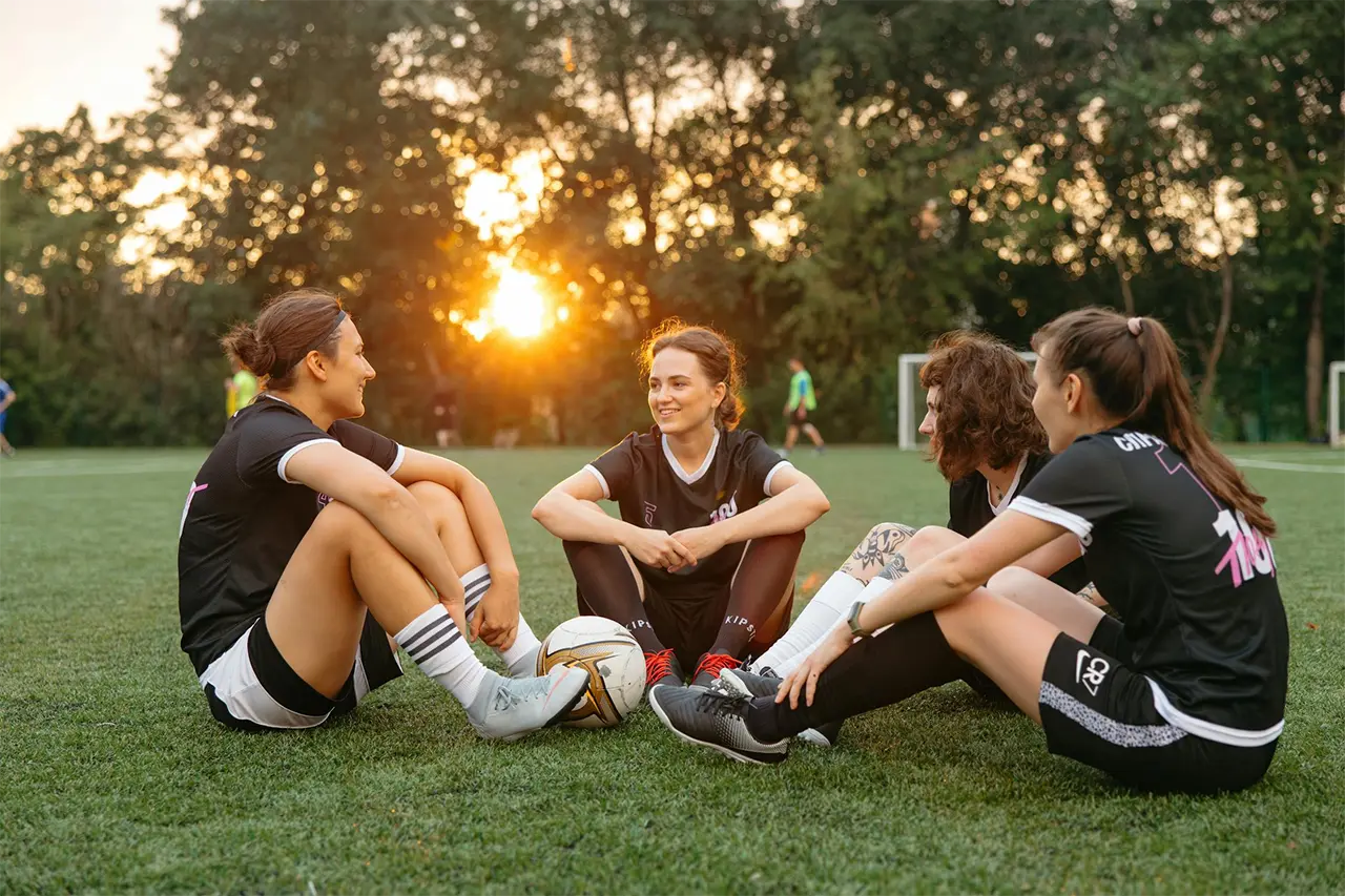 women soccer teammates sitting in a circle on a soccer field