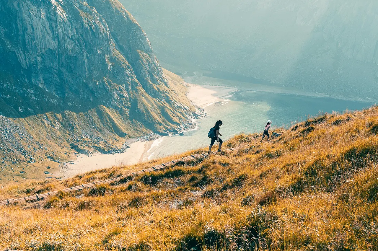young woman and small child climbing a large hill near mountains